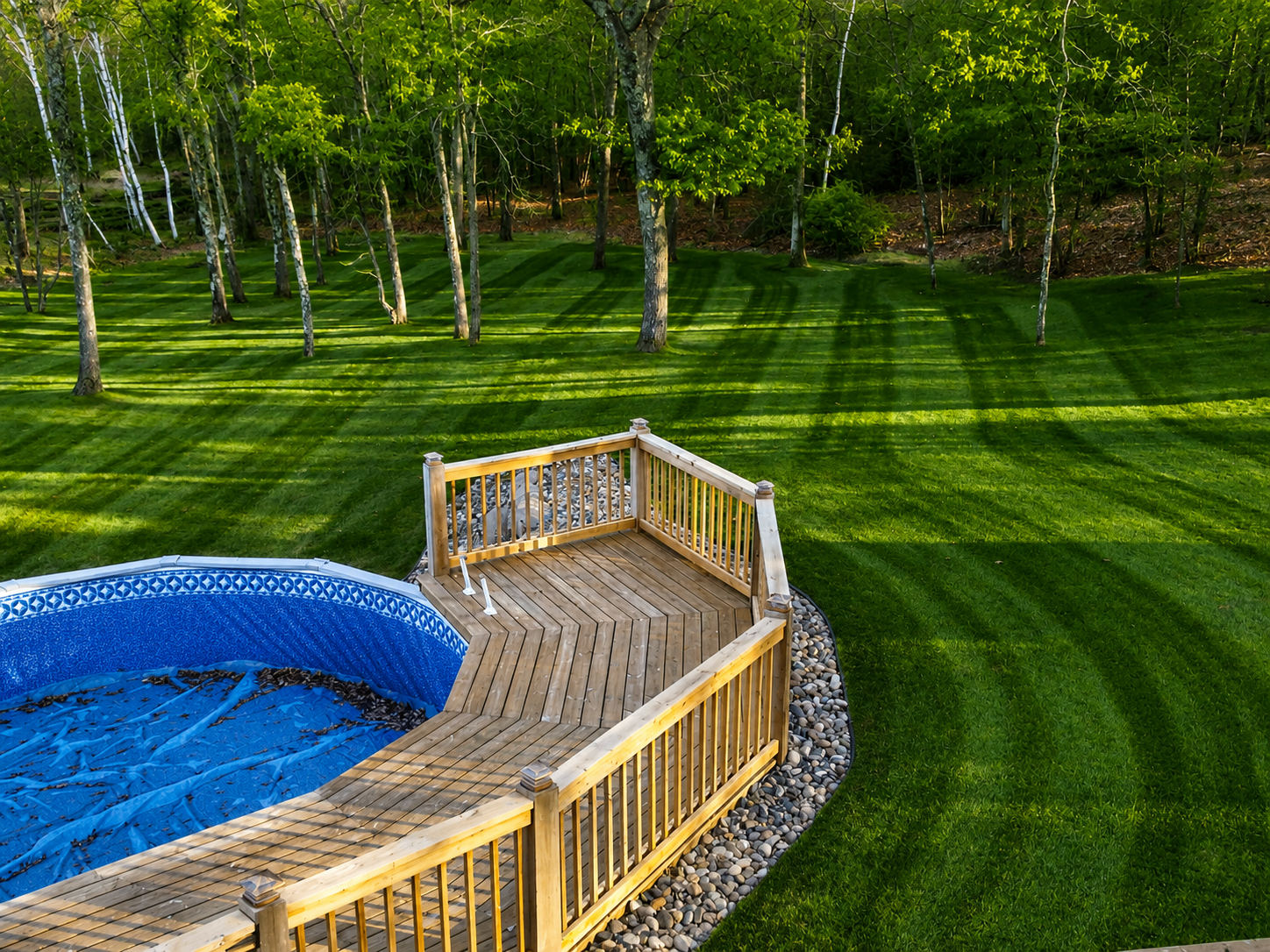 Wooden pool deck surrounded by manicured striped lawn and trees