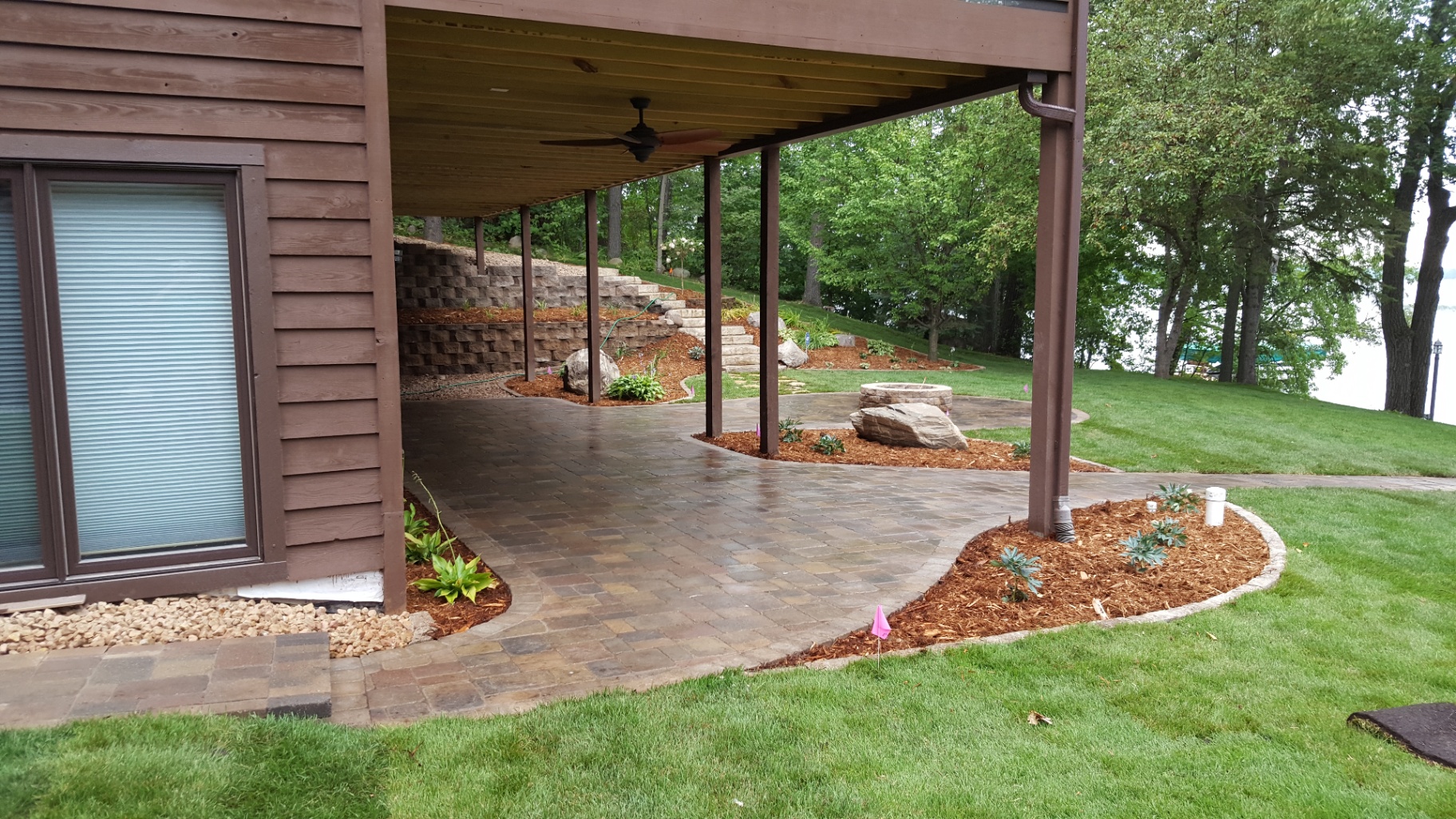 Under-deck paver patio with fire pit and retaining wall overlooking lake